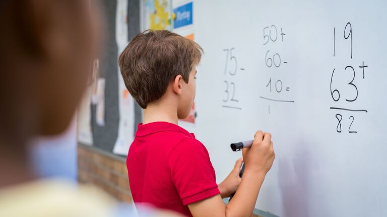 Junge rechnet Mathematikaufgabe an einer Tafel. 
