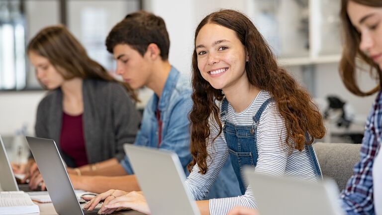 Schülerinnen und Schüler sitzen mit Laptop im Unterricht.